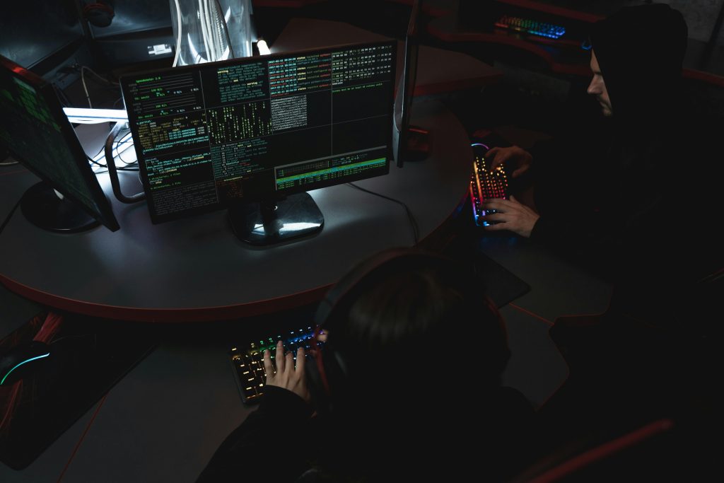 Two people working at computers in a darkened room with multiple screens displaying code