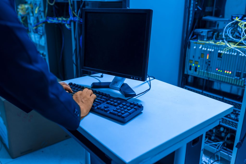 An IT professional operates a computer in a server room, managing network systems and connected devices, representing reactive IT support.