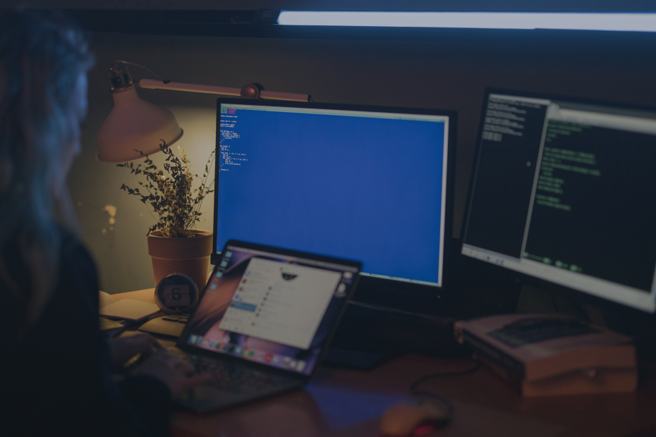 Woman using multiple screens for cybersecurity tasks in a cosy home office