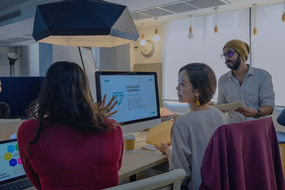 A diverse group of professionals working together in a contemporary office setting using laptops and a monitor.